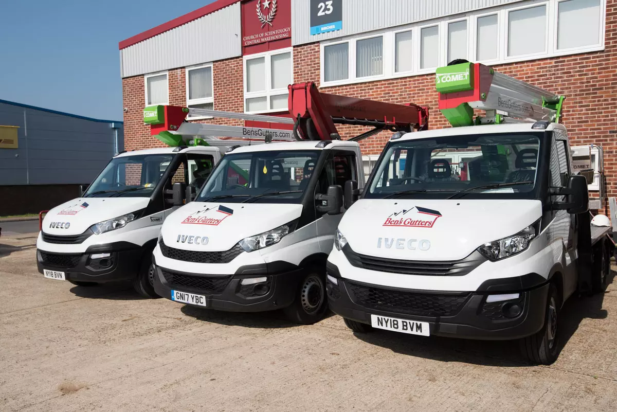 Three vans with roof mounted ladders parked in front of a commercial building