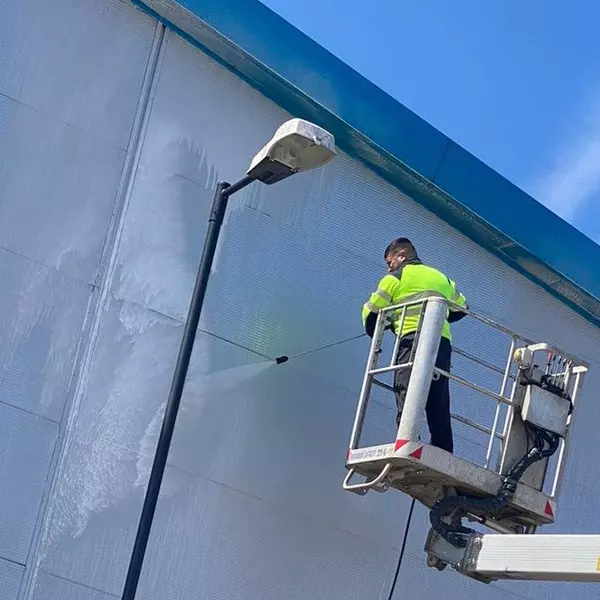 Workman in a cherry picker jet-washing the cladding on a commercial building